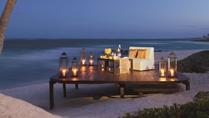 A beachside setup with a wooden table, candles, and a white sofa under palm trees. - Dreams Tulum Resort & Spa - All Inclusive (Tulum)