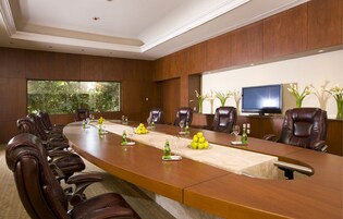 Un salón de conferencias con una mesa larga, sillas de cuero, una televisión y vistas a zonas verdes.