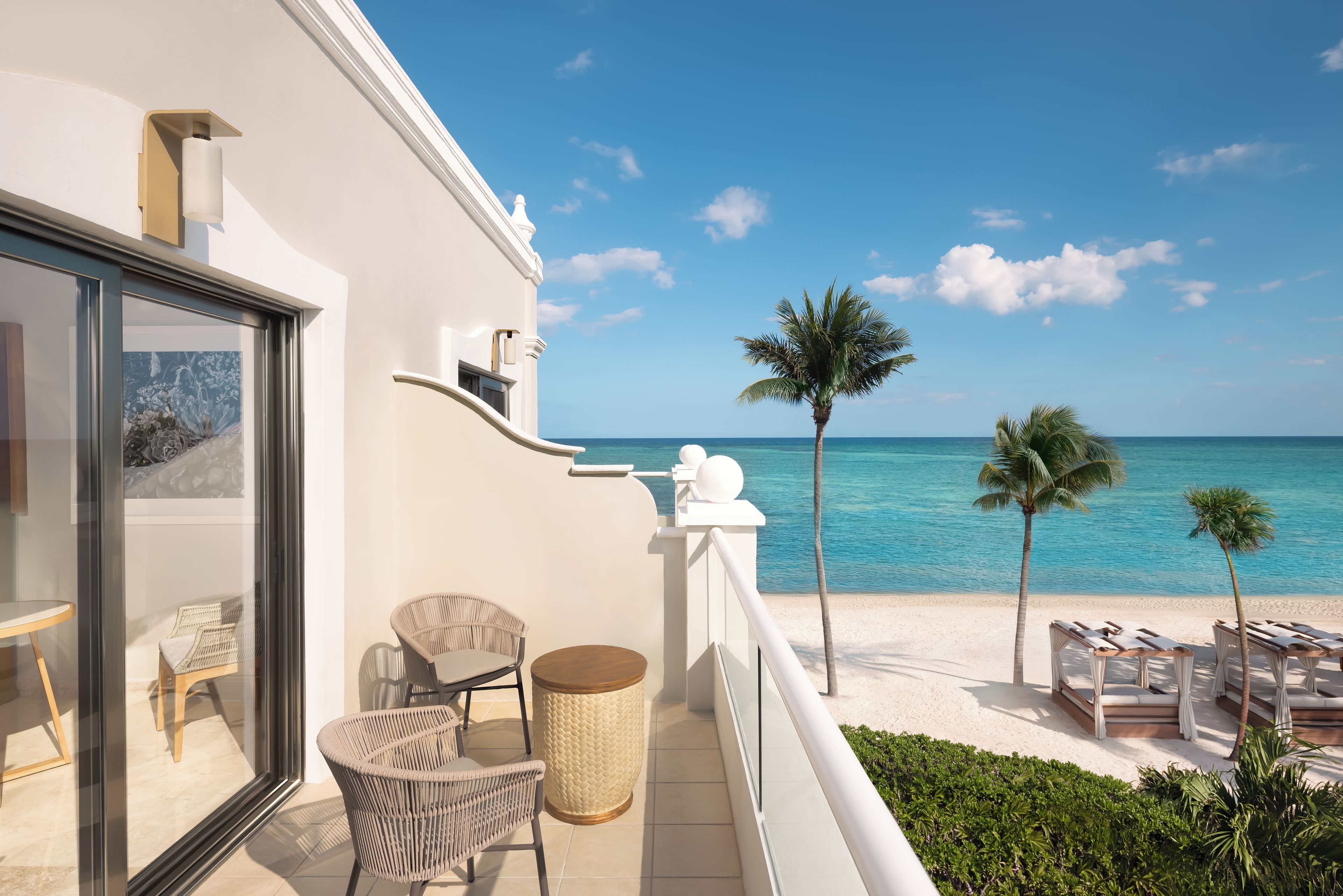 A balcony with wicker chairs, a small table, and a view of the beach and ocean.