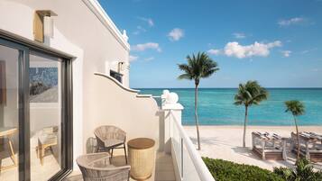 A balcony with wicker chairs, a small table, and a view of the beach and ocean.