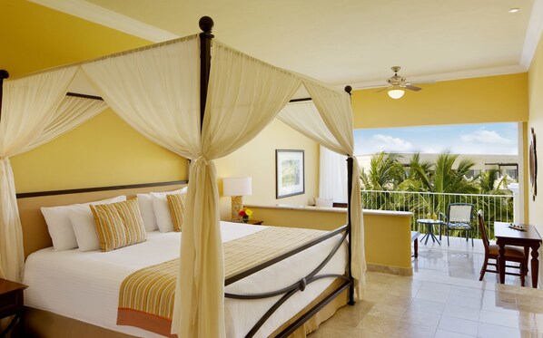 A four-poster bed with a balcony view, a ceiling fan, and a small table with chairs.