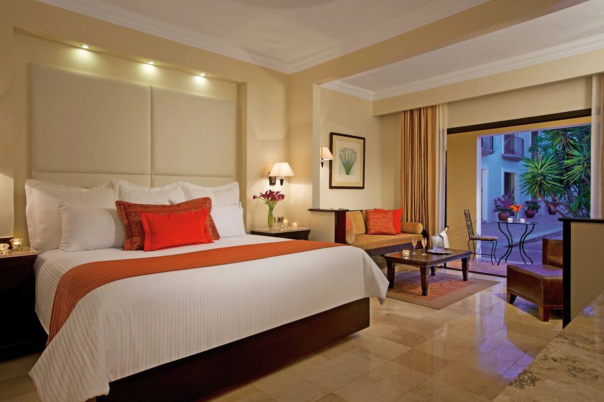 A hotel room with a large bed, a sofa, a coffee table, and a view of the outside.