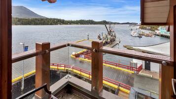 A view from a balcony overlooking a dock with boats, a pier, and a forested mountain in the background.
