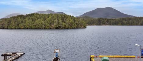 A dock extending into a calm lake with a forested island and mountains in the background.