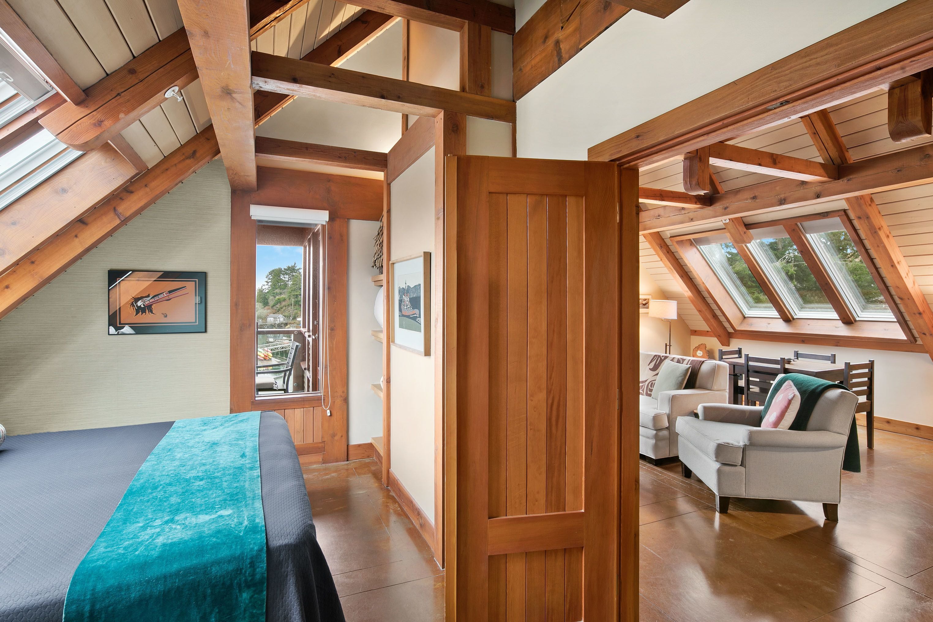 A spacious loft bedroom with a large bed, wooden beams, skylights, and a view of the outdoors.