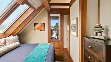 Une chambre avec un plafond en pente, des poutres en bois, un lit avec une literie à motifs, une commode et des œuvres d’art encadrées.