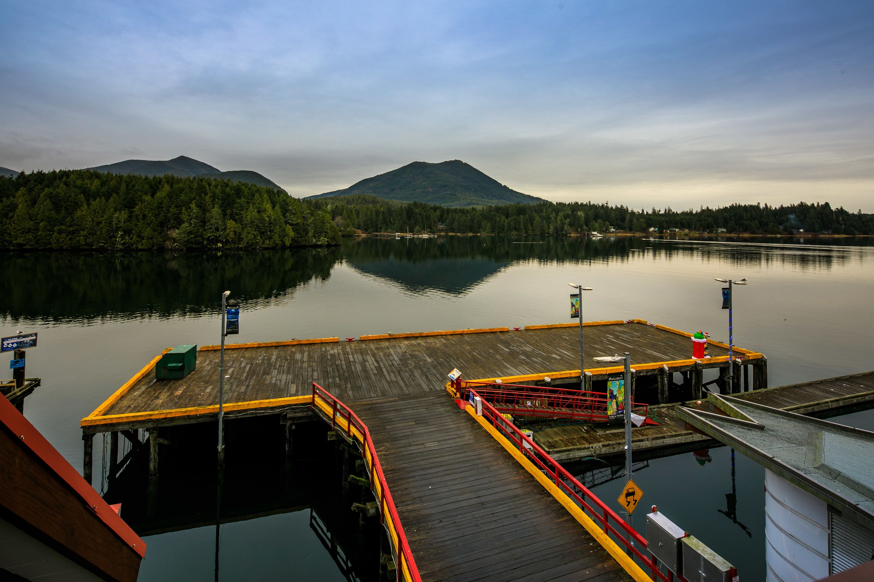 A dock extending into a calm lake with a forested mountain in the background.