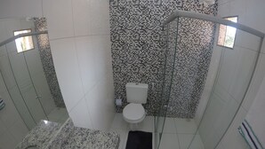 Un baño con ducha envuelta en vidrio, inodoro y lavamanos de granito.