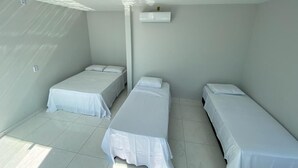 Una habitación con tres camas individuales, un equipo de aire acondicionado blanco en la pared y suelo de baldosas.