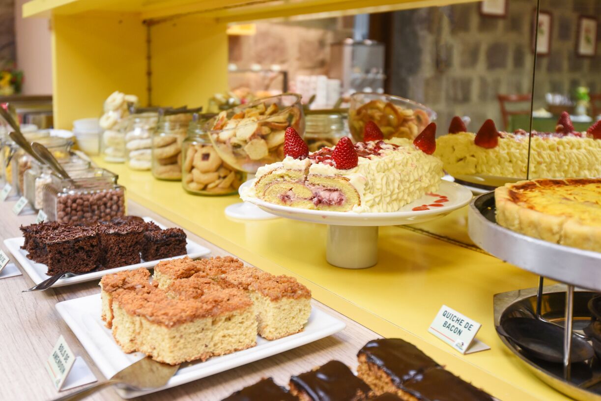 Diverse desserts staan op een toonbank met labels, waaronder een taart met aardbeien en een bordje met de tekst 'QUICHE DE BACON'.
