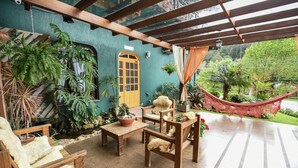 A covered patio area with wooden furniture, potted plants, and a hammock. - Pousada Três Pinheiros (Gramado)