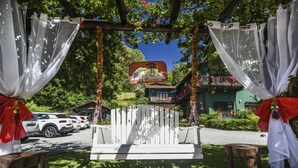 A white swing chair under a canopy with a sign reading "Paseo de los Inmigrantes" in front of a building with balconies. - Pousada Três Pinheiros (Gramado)