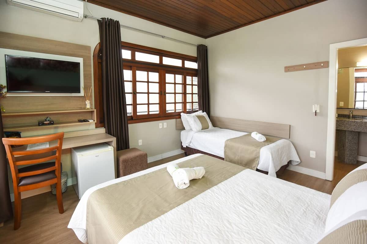 A hotel room with a bed, a desk, a chair, a TV, and a window with curtains.