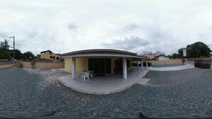A building with a covered patio area, a gravel driveway, and a few parked cars. - Pousada Parque Praia (Penha)