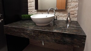 A bathroom with a white vessel sink, a granite countertop, a mirror, and a small plant. - Hotel Mica (Abancay)