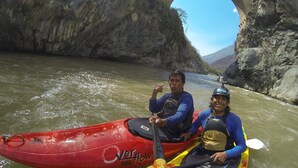 Two people in a red and yellow kayak on a river with a bridge in the background. - Hotel Mica (Abancay)
