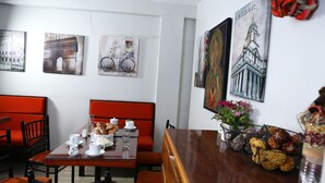 A dining area with a wooden table set for two, red upholstered chairs, and artwork depicting Paris and London on the walls. - Hotel Mica (Abancay)