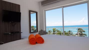 Een hotelkamer met een groot bed, een flatscreen televisie aan de muur, een groot raam met uitzicht op de oceaan, en twee opgerolde handdoeken op het bed.