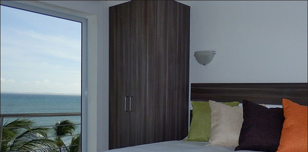 A bedroom with a large window, a bed with multiple pillows, and a wooden wardrobe.