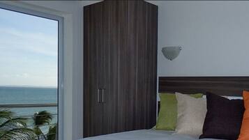 Een slaapkamer met een groot raam, een bed met veel kussens en een houten garderobe.