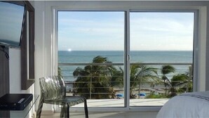 A room with a large sliding glass door leading to a balcony with a view of the ocean and palm trees. - Yaque Beach Hotel (Díaz)