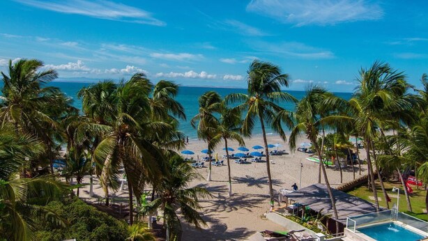 A beach view with palm trees, a pool, and beach umbrellas. - Yaque Beach Hotel (Díaz)