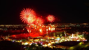 A nighttime view of a cityscape with fireworks, illuminated buildings, and a densely packed urban area. - Monki-Di Executive Suites - Alura (Calgary)