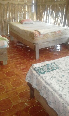 A room with two beds, a wooden floor, and a bamboo wall. - Cabañas Ukuptupu (Narganá)