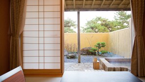 Una habitación japonesa tradicional con suelo de tatami, un celosía shoji y vistas a un jardín con un árbol bonsái y un banco de madera.