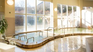 Una amplia piscina cubierta con ventanales de vidrio, barandillas metálicas y suelo de baldosas.