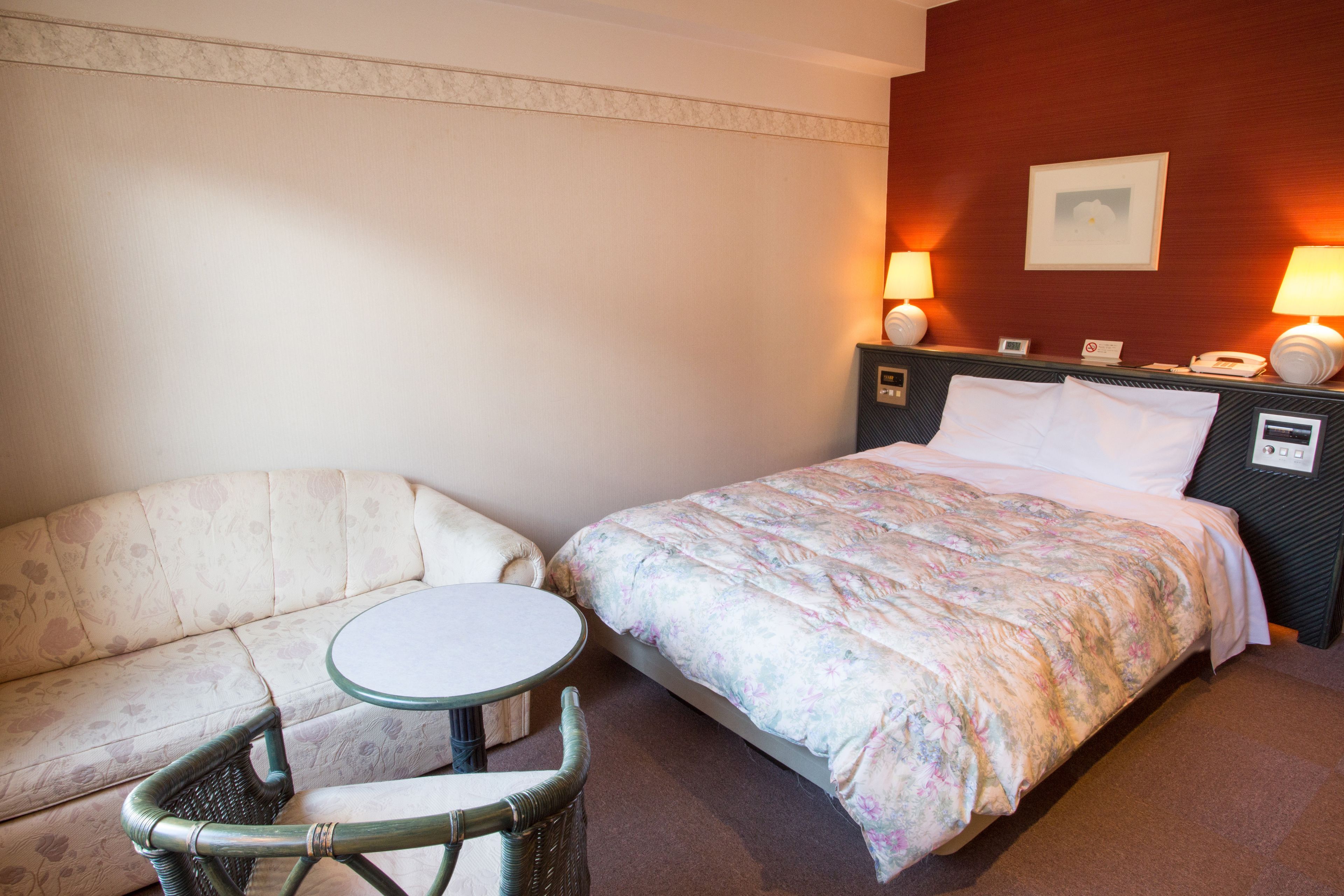 A hotel room with a bed, a sofa, a small round table, and two bedside lamps.
