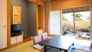 Una habitación tradicional japonesa con suelo de tatami, una mesa baja y un televisor sobre un mueble.