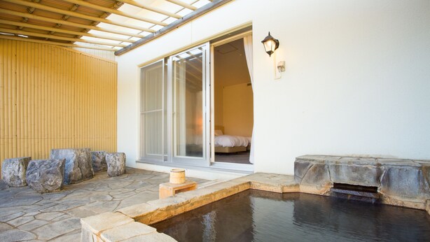 Una piscina de piedra con cubierta de madera, puerta corrediza de vidrio que da a un dormitorio y pared de piedra con valla de listones de madera.