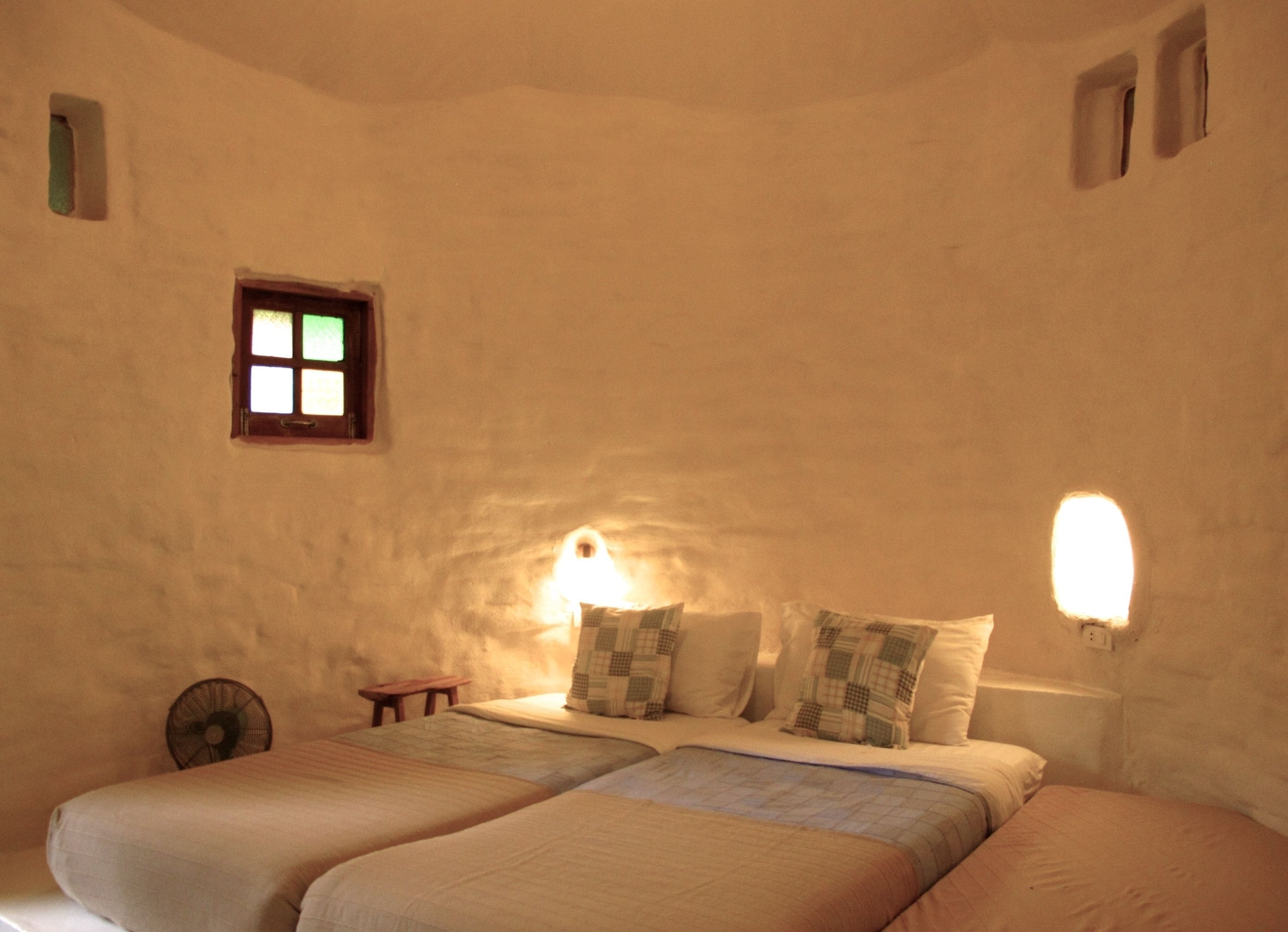 Una habitación con techo bajo, cama con dos almohadas, una mesita y un ventilador.
