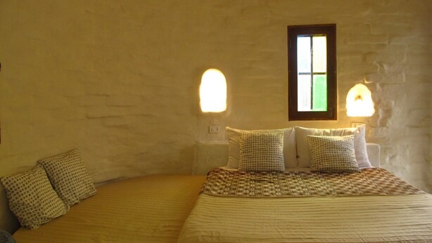 Un dormitorio con cama, dos mesitas de noche, una ventana y luces fijadas a la pared.