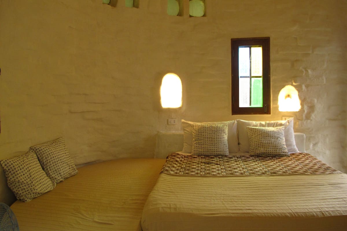 A bedroom with a bed, two nightstands, a window, and wall-mounted lights.