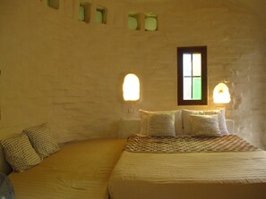 Une chambre à coucher avec un lit, deux tables de chevet, une fenêtre et des lampes fixées au mur.