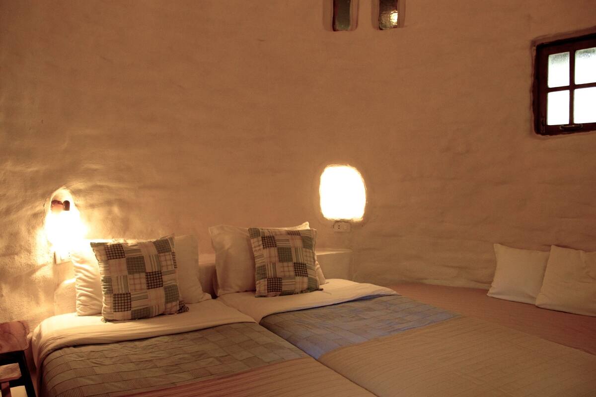 A cozy room with two beds, a small window, and a wall-mounted light fixture.