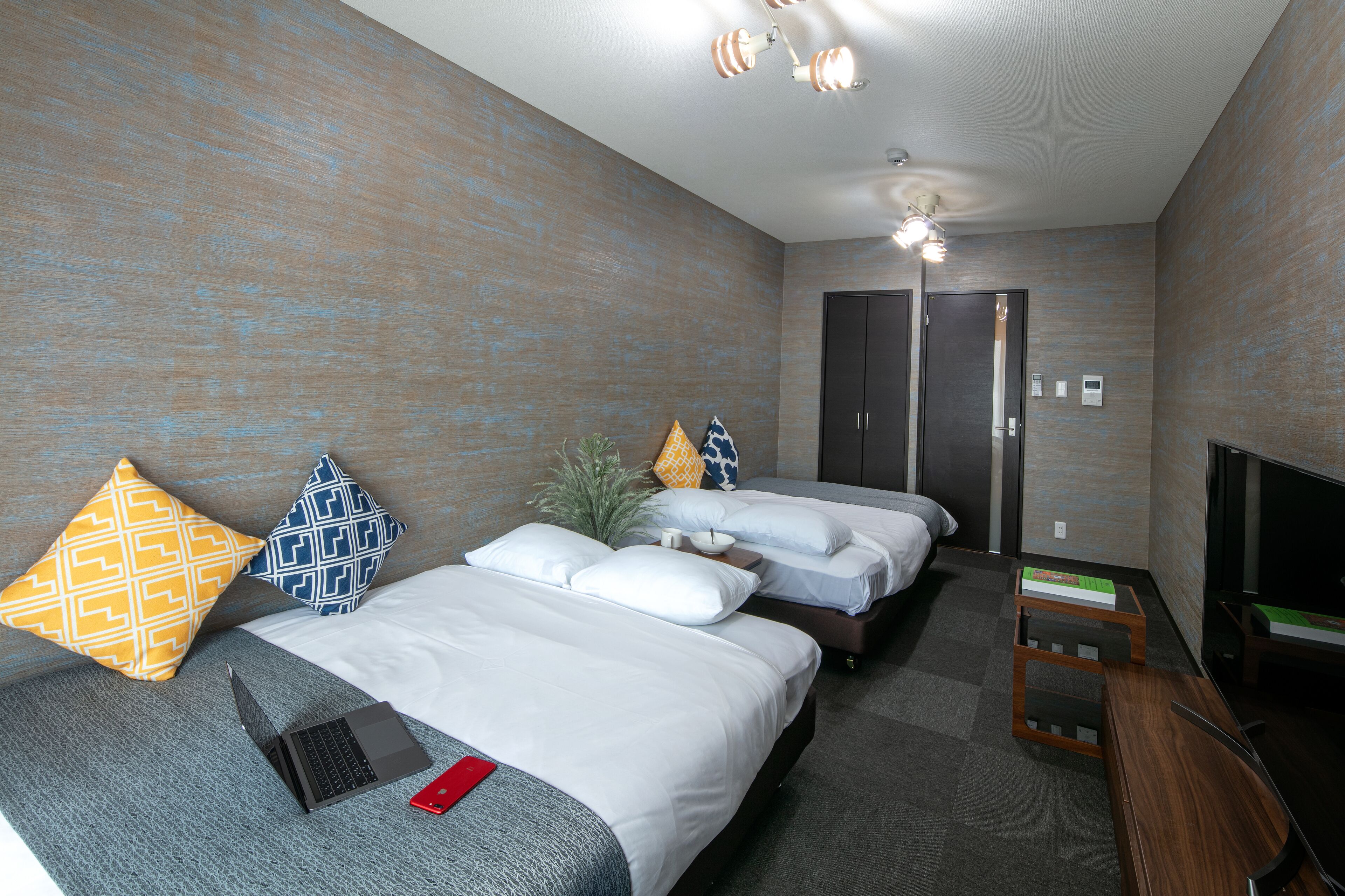A hotel room with two beds, a desk with a laptop, a TV, and a door leading to a bathroom.