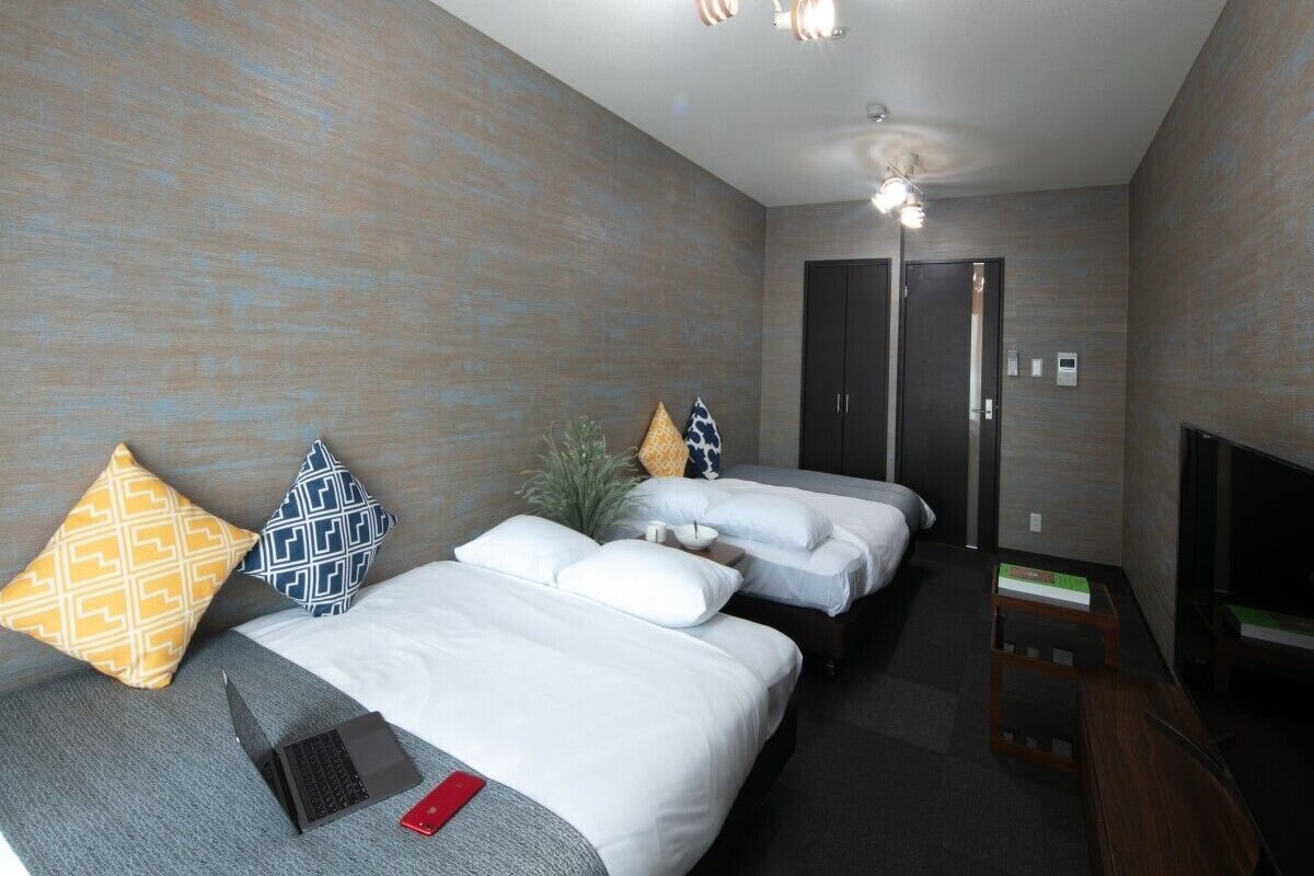 A hotel room with two beds, a TV, a desk, and a fireplace.