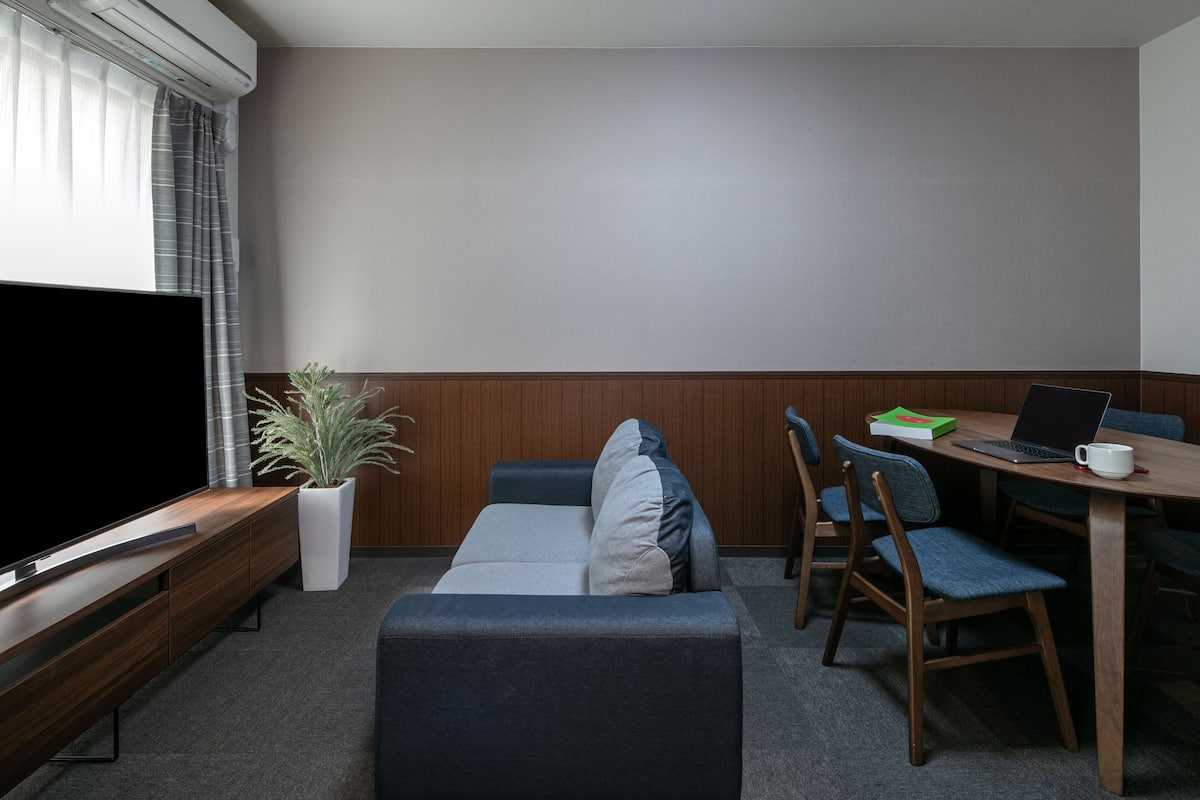 Un salon moderne avec un téléviseur à écran plat, un canapé, une table à manger avec des chaises et une plante en pot.