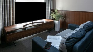 Un salon moderne avec un téléviseur à écran plat, un meuble de rangement en bois, une plante en pot, un canapé et un livre posé sur une table basse.