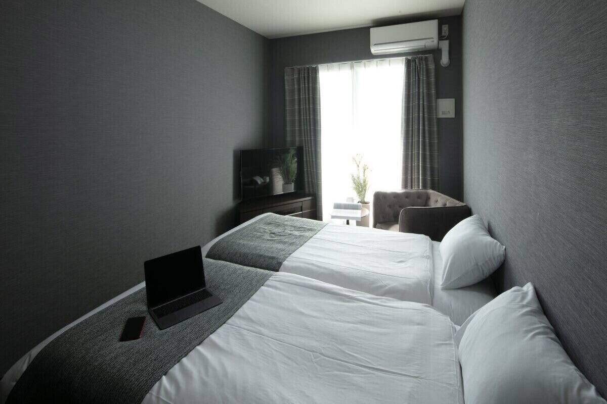 Une chambre d’hôtel avec deux lits, un ordinateur portable sur le lit de gauche, un téléviseur au mur et une fenêtre avec des rideaux.