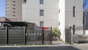 Une entrée fermée par un portail mène à un immeuble sur lequel on peut lire l’inscription suivante : « RÉSIDENCE RANDOR, STYLE KYOTO ».