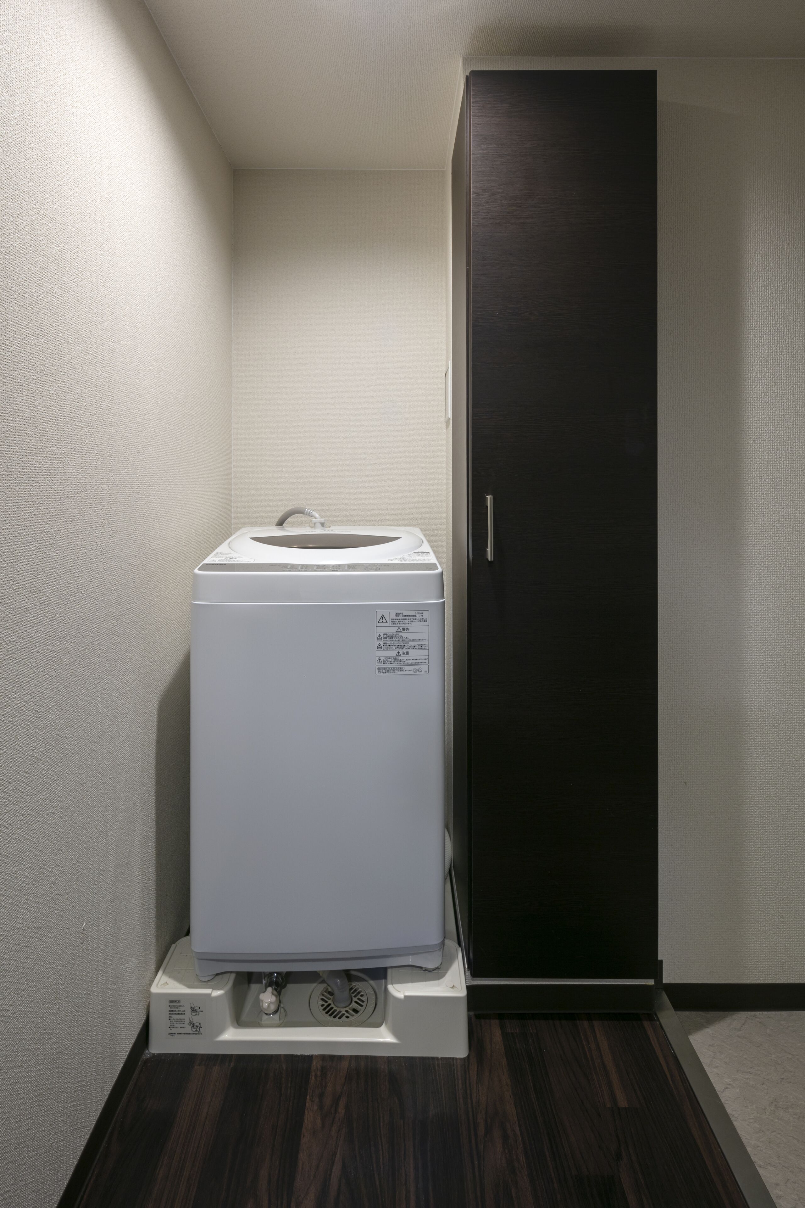 A compact room with a white washer and dryer unit, a dark wooden cabinet, and a textured wall.