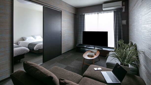Une chambre d’hôtel moderne avec un canapé, un ordinateur portable, une petite table avec une plante et un lit équipé d’un téléviseur.