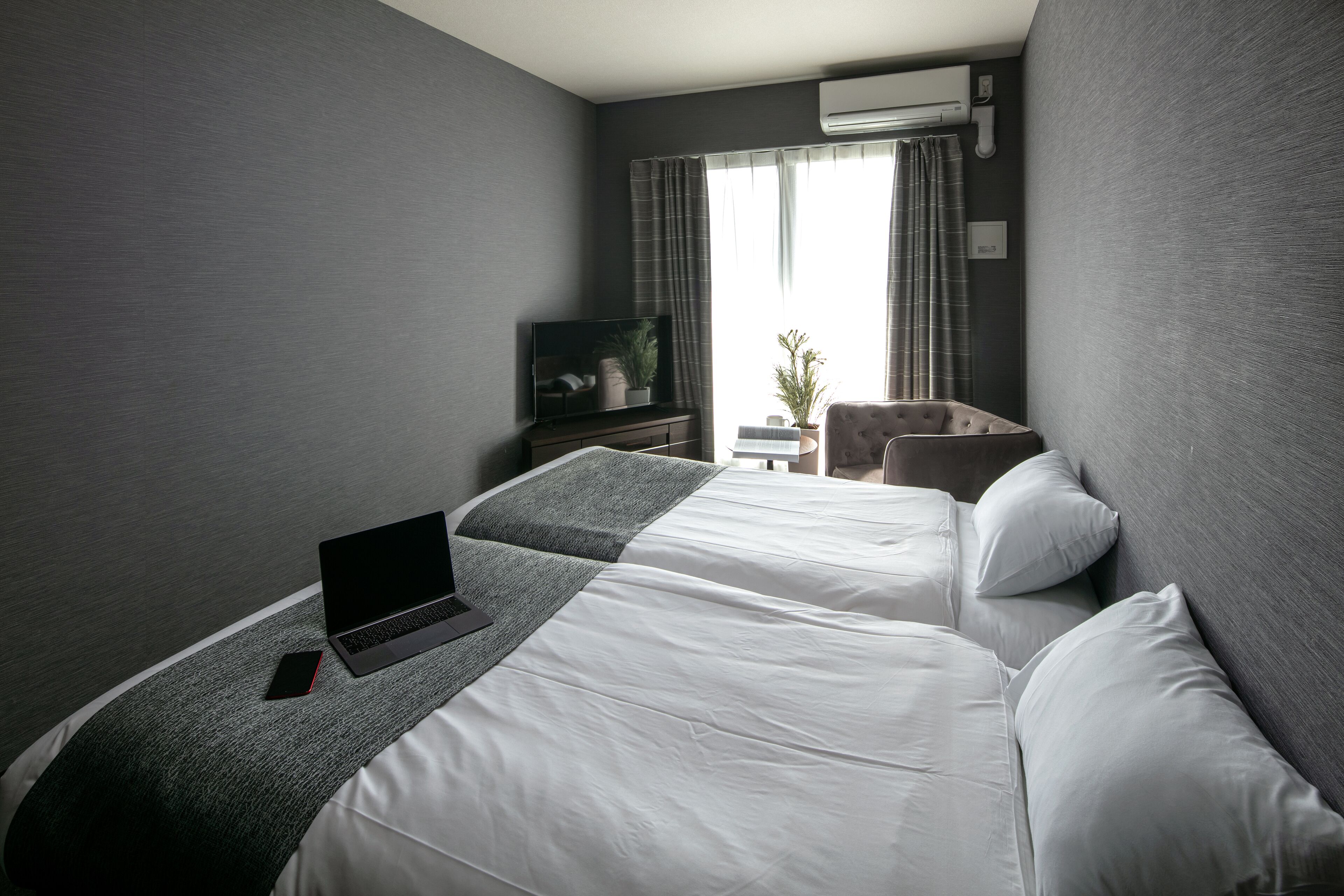 A hotel room with two beds, a laptop, a TV, and an air conditioning unit.