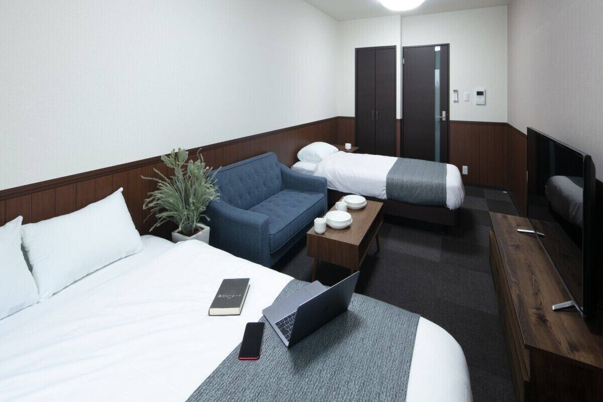 Une chambre d’hôtel comprenant un lit, un bureau avec un ordinateur portable, une chaise, un canapé, une télévision et une armoire.