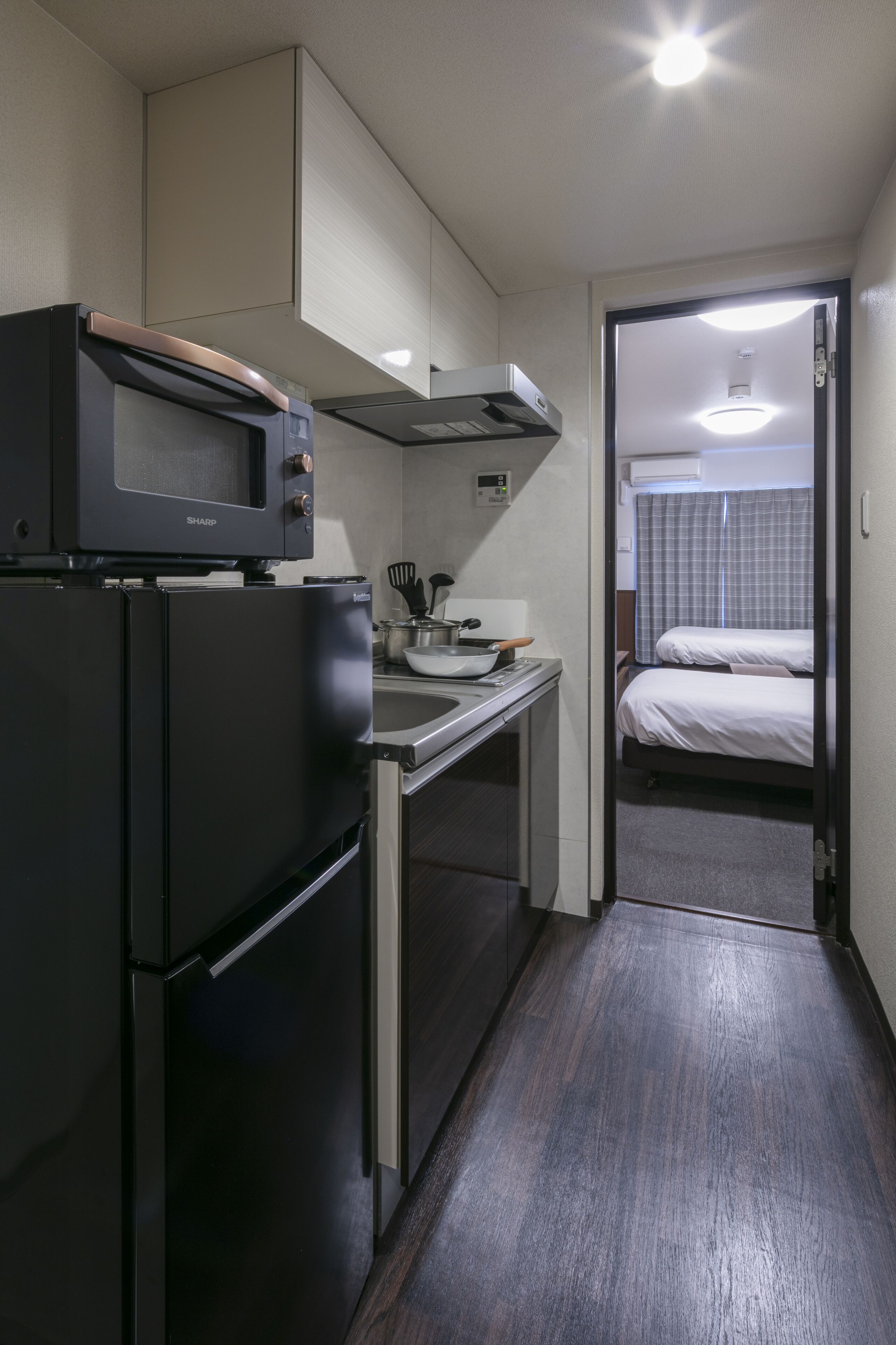 A compact kitchen with a microwave, refrigerator, and sink. A small dining area is visible with a table and chairs. A doorway leads to a bedroom with a bed.