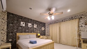 Un dormitorio con una cama de madera, una mesita de noche, una lámpara, un ventilador de techo y papel tapiz floral.